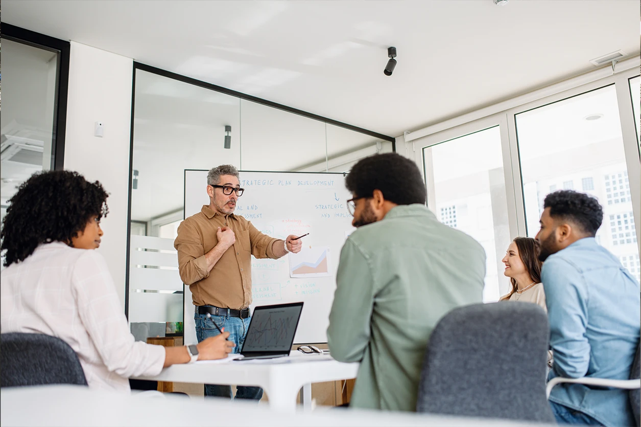 A middle-aged business professional delivers a compelling presentation. A diverse audience of employees is actively engaged, highlighting teamwork, leadership, and business development.